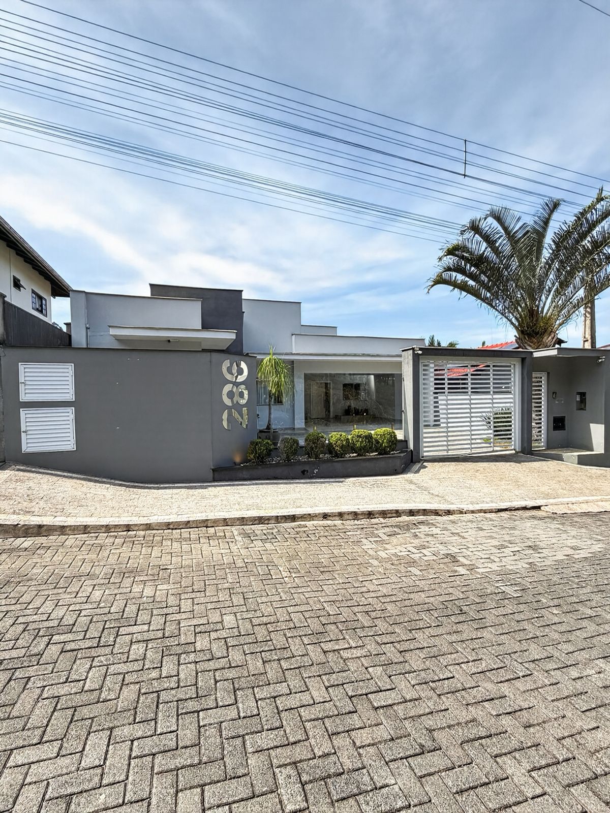 Fachada da casa vista da rua, com muro cinza, portão branco e garagem coberta